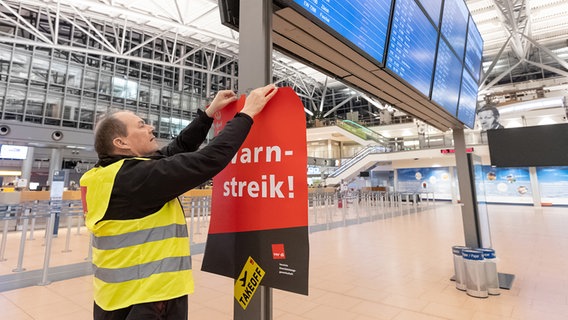 A Verdi representative hangs a poster with the inscription “Warning Strike” in a terminal at Hamburg Airport.  © picture alliance/dpa |  Bodo Marks Photo: Bodo Marks