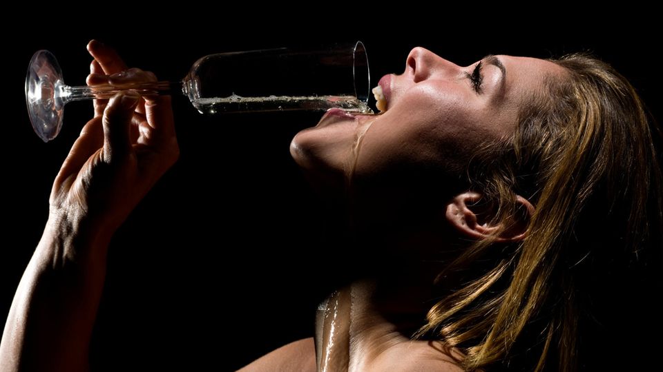 A woman pours a glass of champagne into her mouth