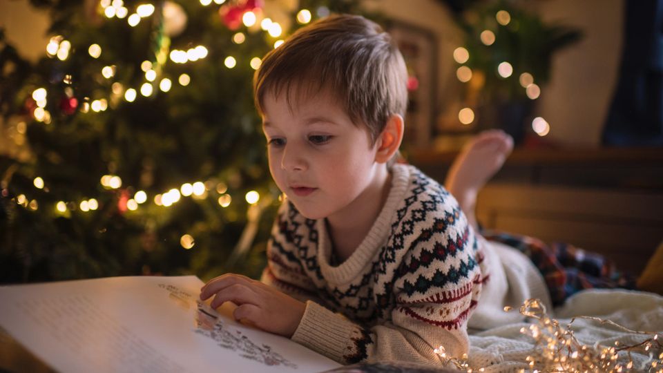 A boy reads a book by the Christmas tree