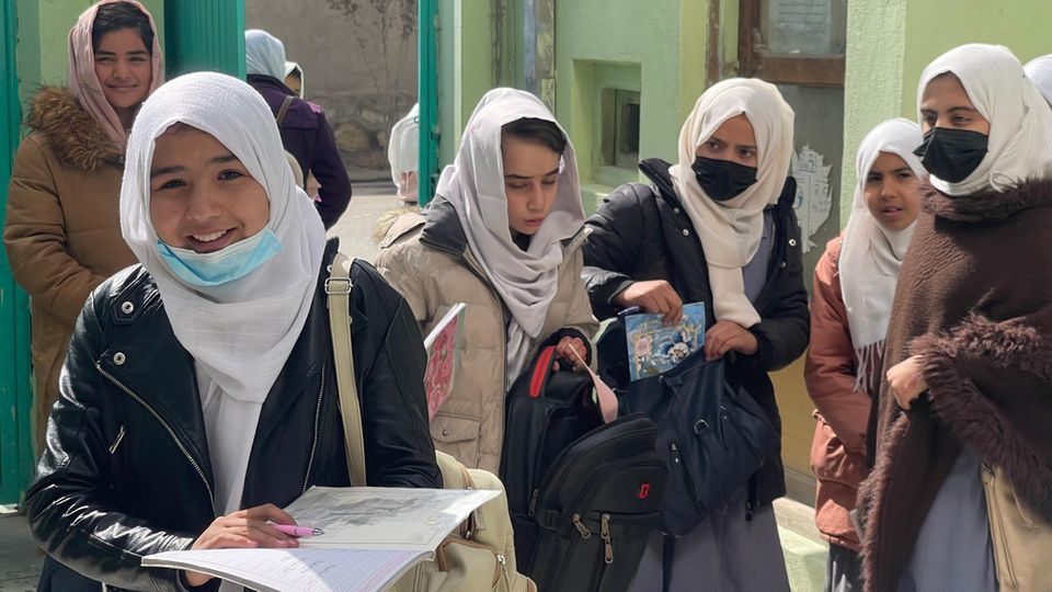 Afghan schoolgirls with books stand in front of a building and talk.