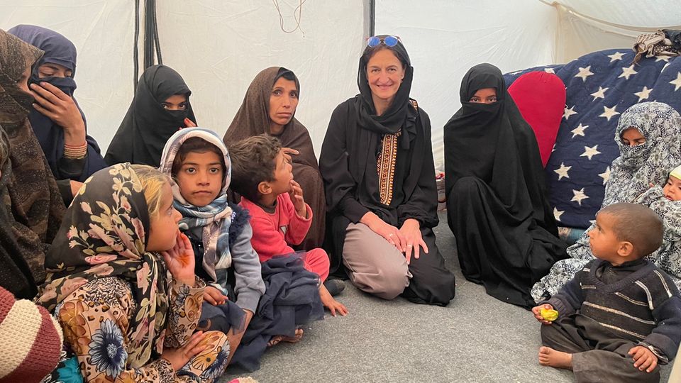 Development worker Christina Ihle kneels in the tent next to Afghan children and family members.