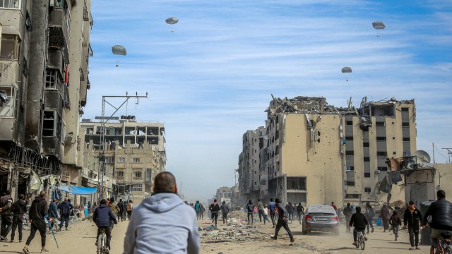 Gaza War: Palestinians walk down a street as humanitarian aid is dropped in Gaza City on March 1.
